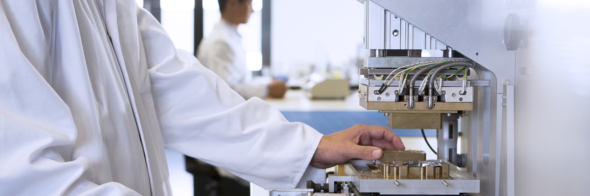 scientist in lab coat operating automated testing machine in bright laboratory setting with colleague in background