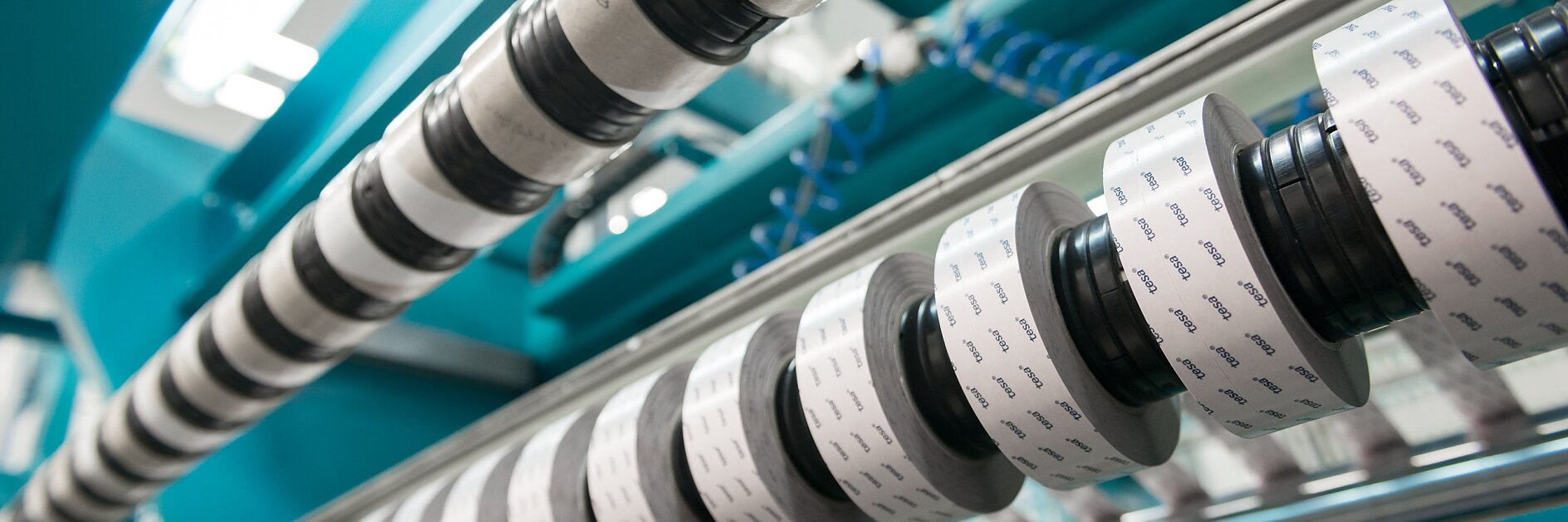 rolls of black and white adhesive tape on a blue industrial machine in a manufacturing setting