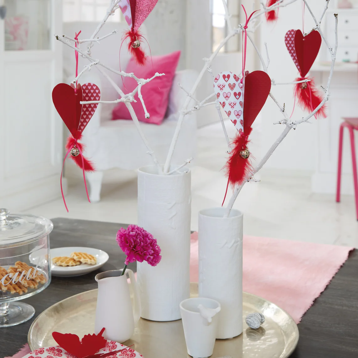 Homemade paper hearts hang in the bouquet made of branches painted white for Valentine's Day.