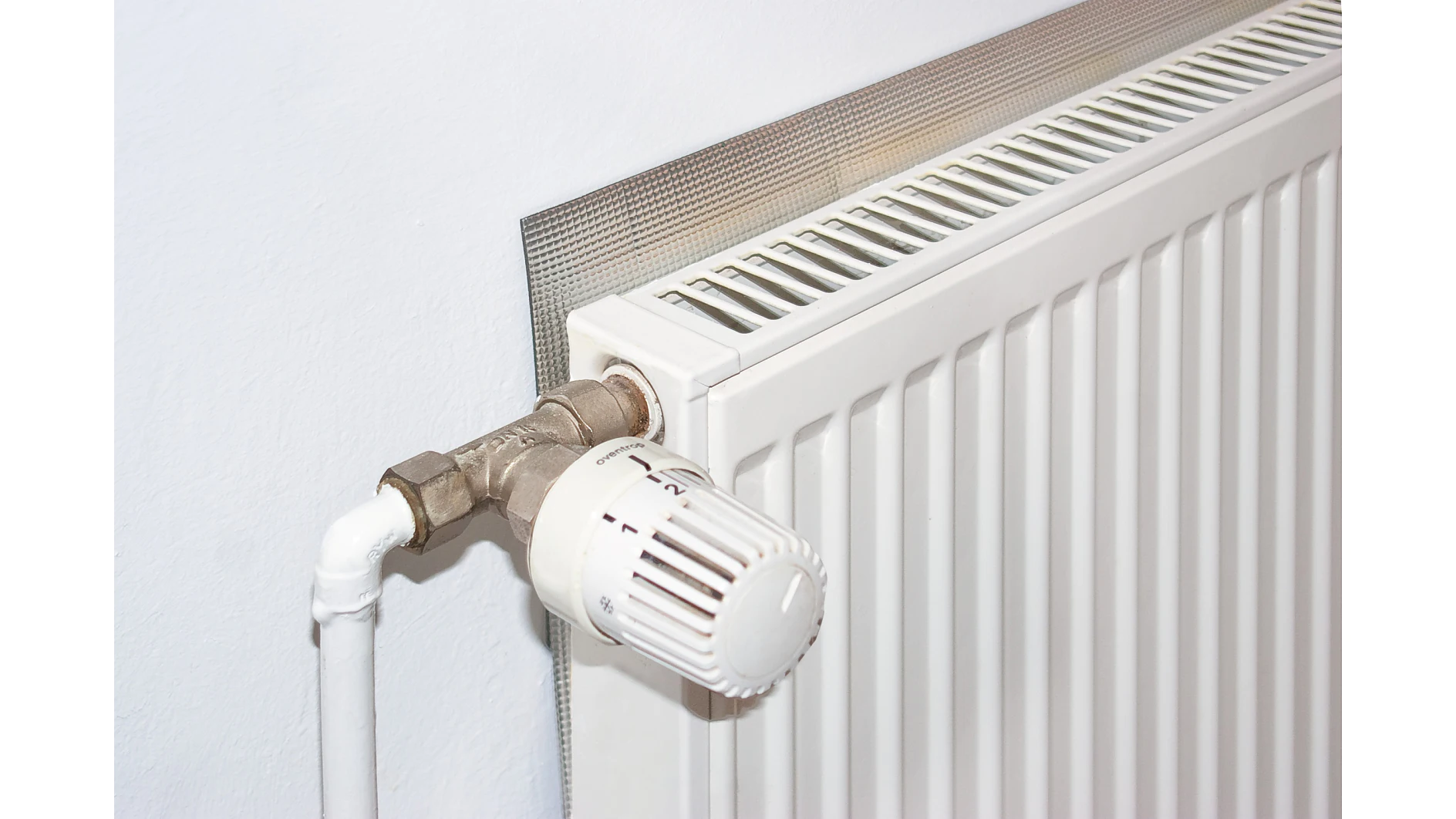 tesa_55157_ap_006_fullsize Close-up of a white radiator with a thermostatic valve, fitted against a wall, with a reflective insulation panel positioned behind it.