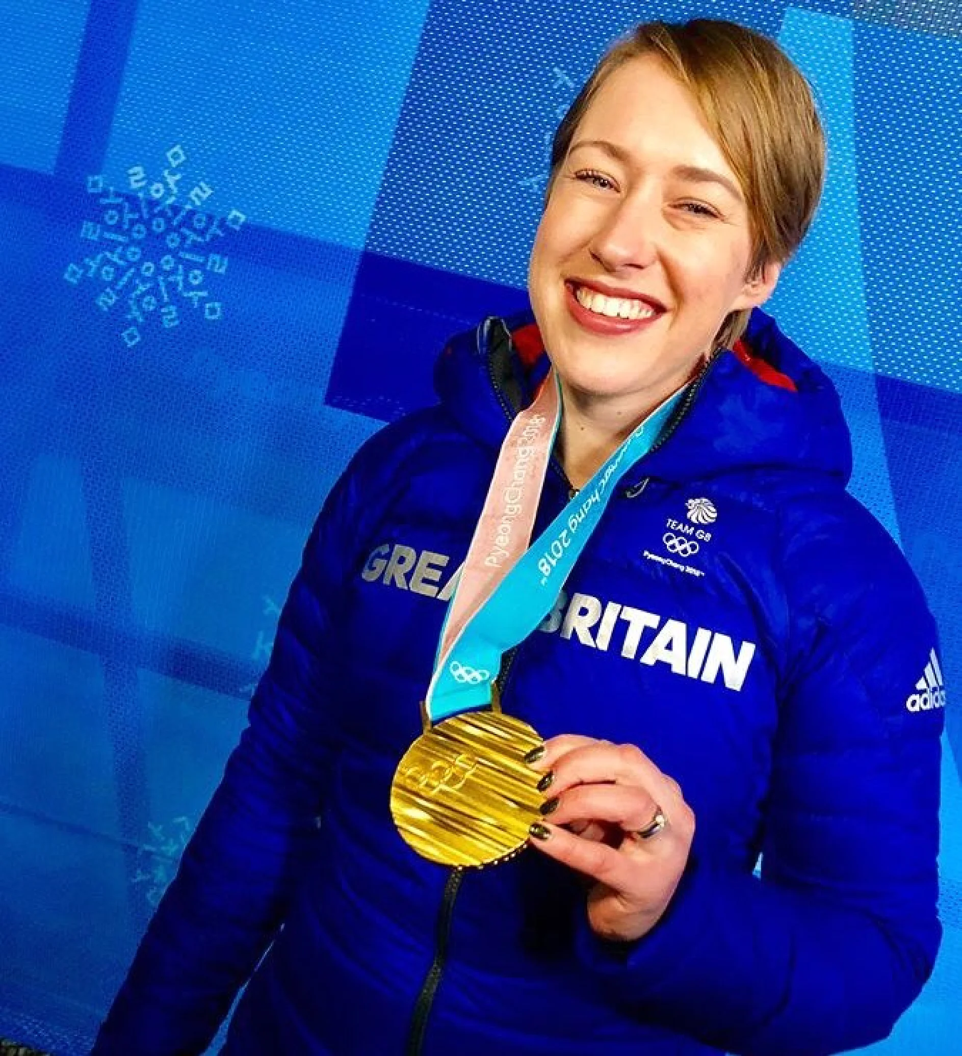 A person wearing a blue jacket that says Great Britain holds a gold medal and smiles. The background is blue with snowflake patterns and faded text. (This text has been generated by AI)