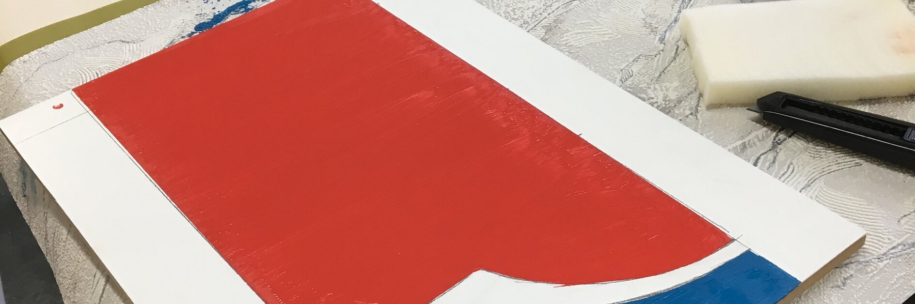 A worktable with art supplies, including tesa tape, paint containers, and paintbrushes. A partially completed painting on paper features red, blue, and white sections. A stencil with the word Pepsi is visible in the background.