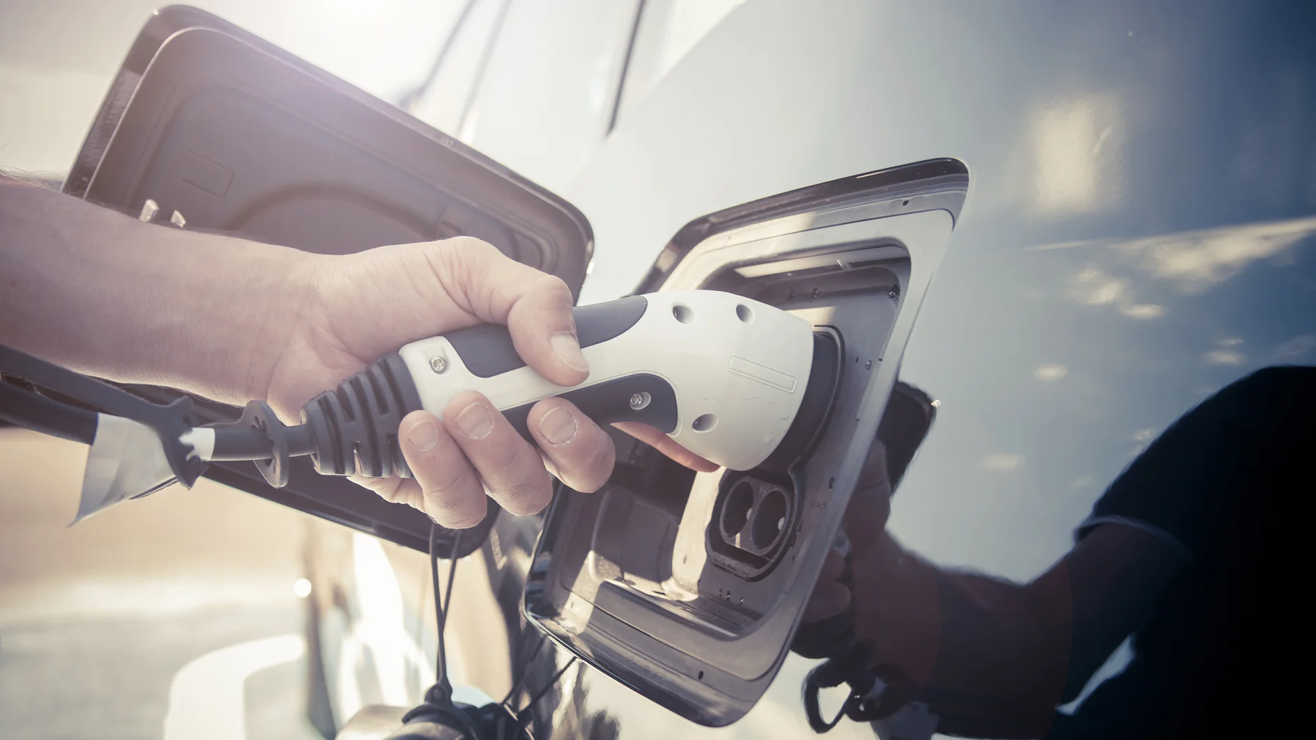 Color image of a man's hand preparing to charge an electric car.