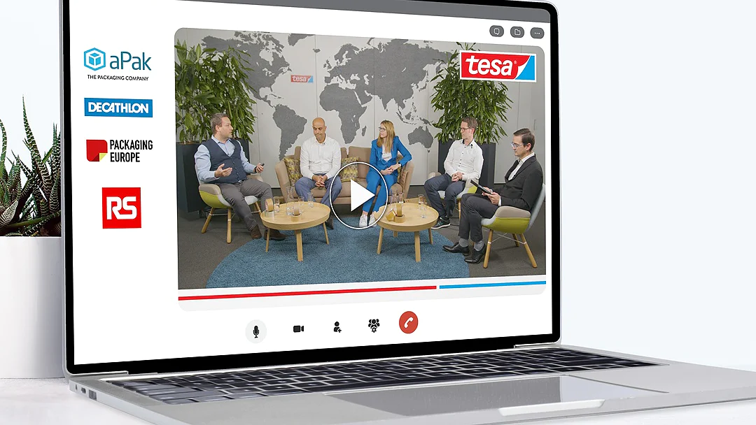 A laptop displays a virtual panel discussion with five people seated in a semi-circle. Logos of aPak, tesa tape, Decathlon, Packaging Europe, and RS appear on the screen. A large world map and plants are in the background. (This text has been generated by AI)