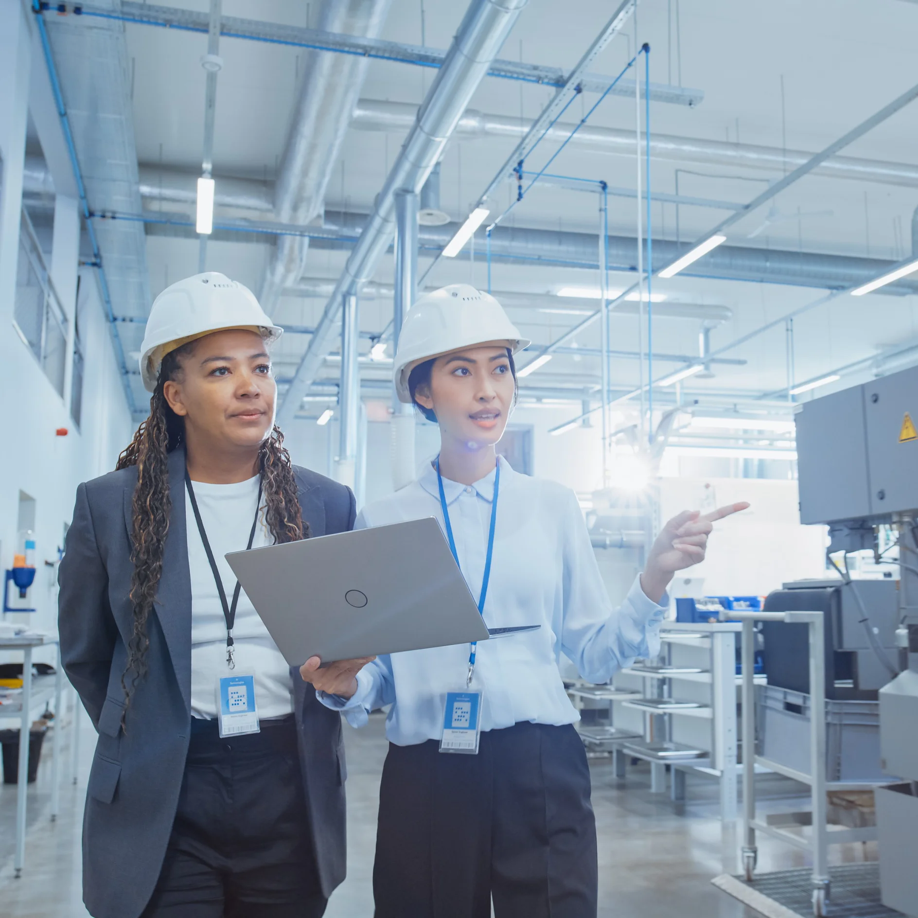 Two Professional Heavy Industry Employees in Hard Hats at Factory. Checking and Discussing Industrial Facility, Working on Laptop Computer. African American Engineer and Asian Technician at Work.