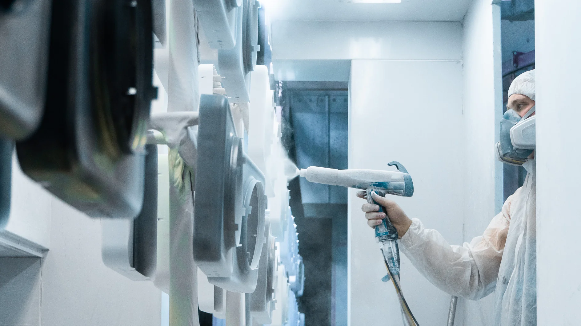 Powder coating of metal parts. Man in a protective suit sprays white powder paint from a gun on metal products Powder coating of metal parts. Man in a protective suit sprays white powder paint from a gun on metal products