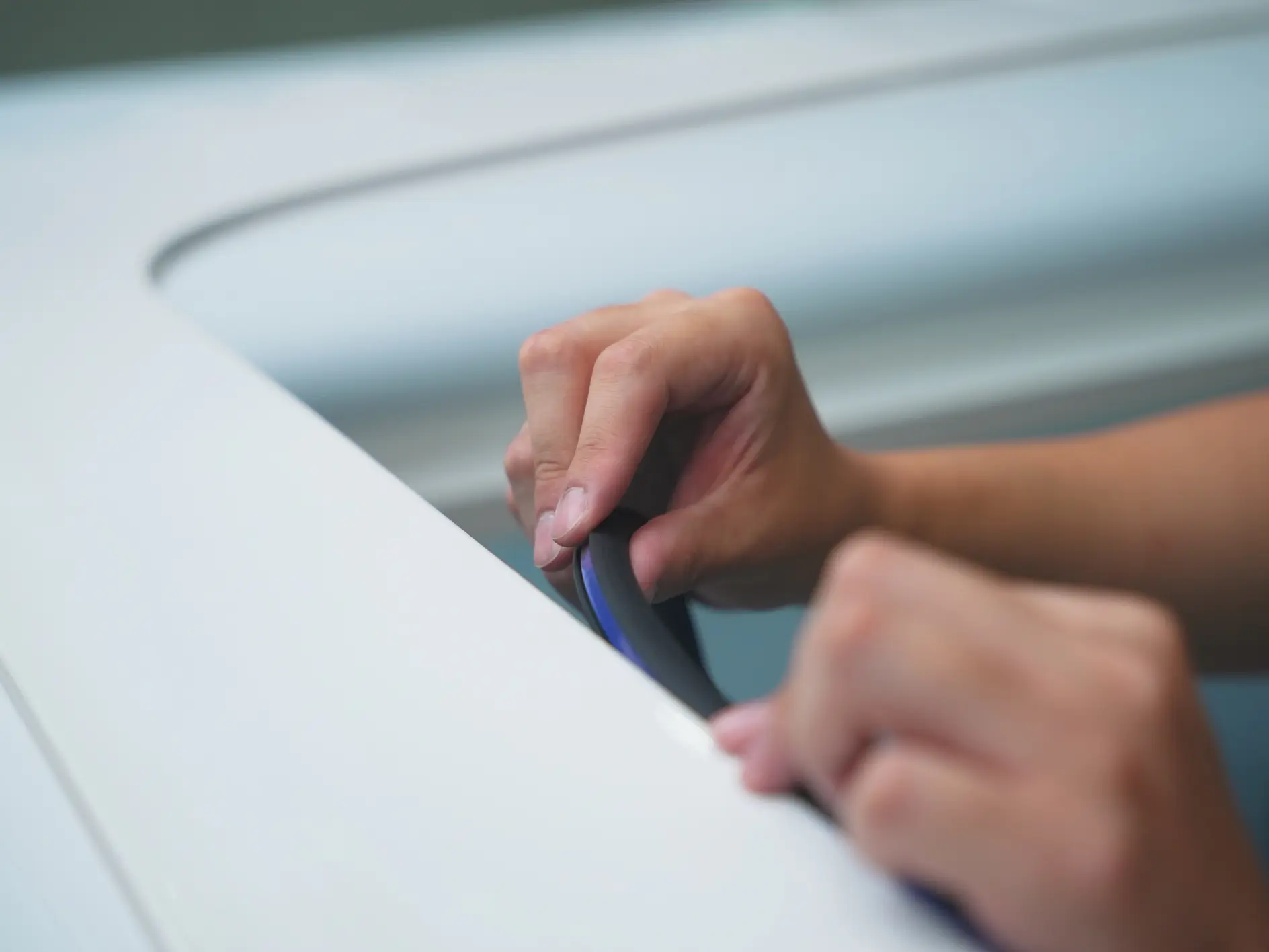 Close-up of two hands applying or smoothing a strip of tesa tape onto a flat, white surface, likely during installation or repair.