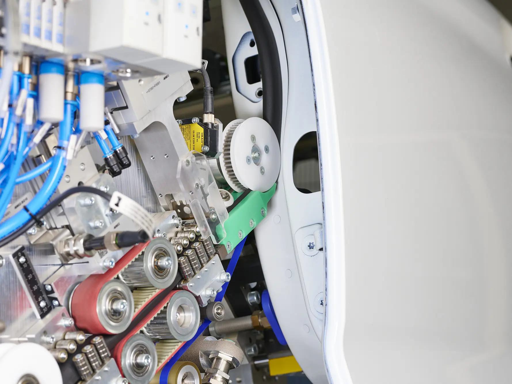 Close-up of industrial machinery featuring belts, pulleys, gears, and cables, with tesa tape visible near a white curved metal surface.