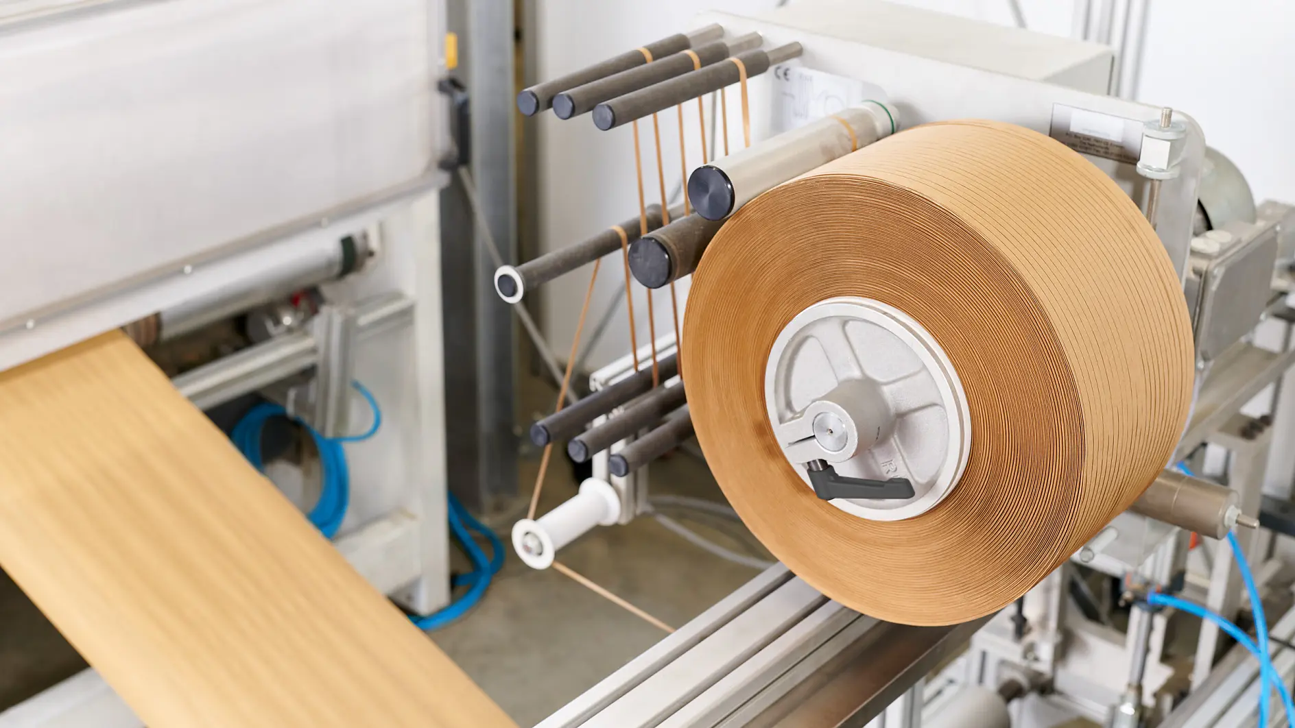 roll of brown packing tape mounted on dispenser in industrial packaging area with conveyor belt and tools nearby