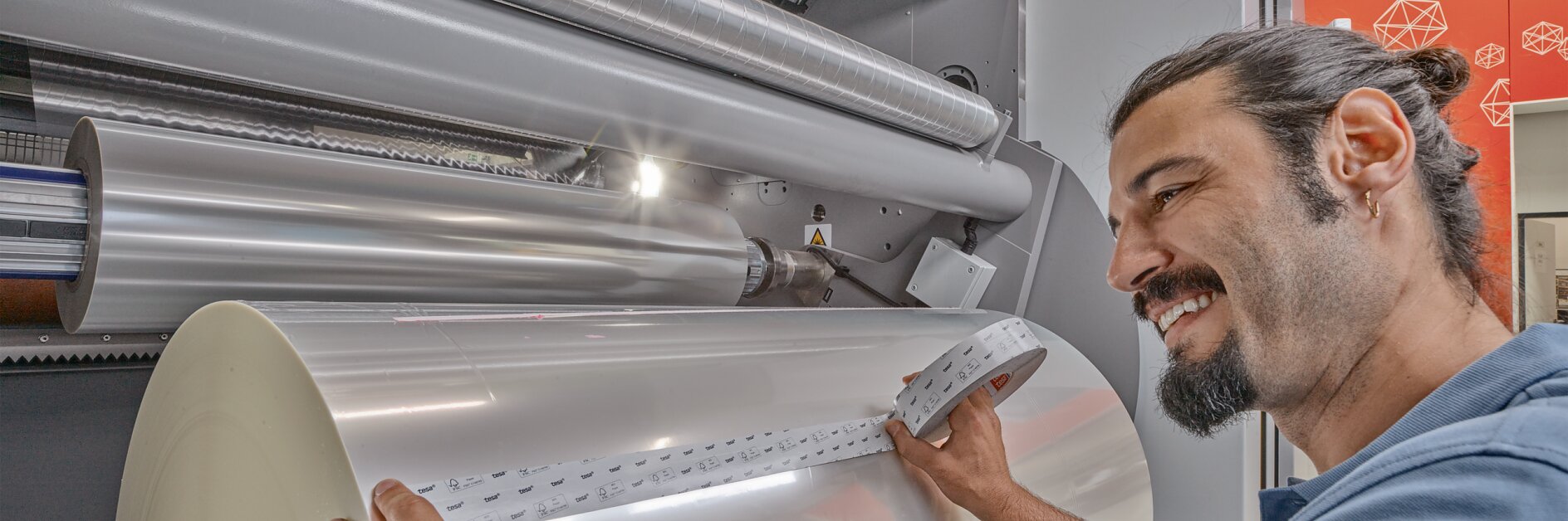 man operating large industrial machine rolling clear plastic film in factory setting