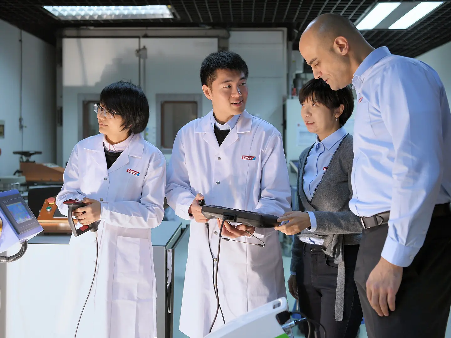 tesa team in lab coats and business attire discussing data on tablets in a modern indoor laboratory setting (This text has been generated by AI)