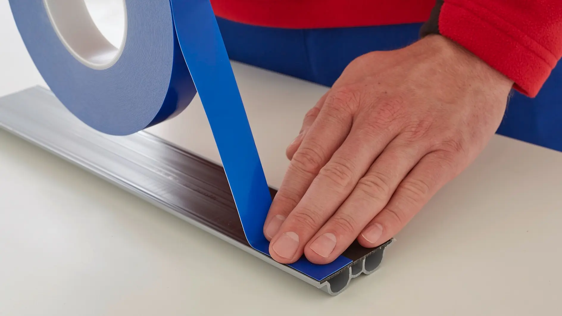 Hand applying blue tesa tape onto a flat surface indoors, focusing on precise placement and smooth adhesion.