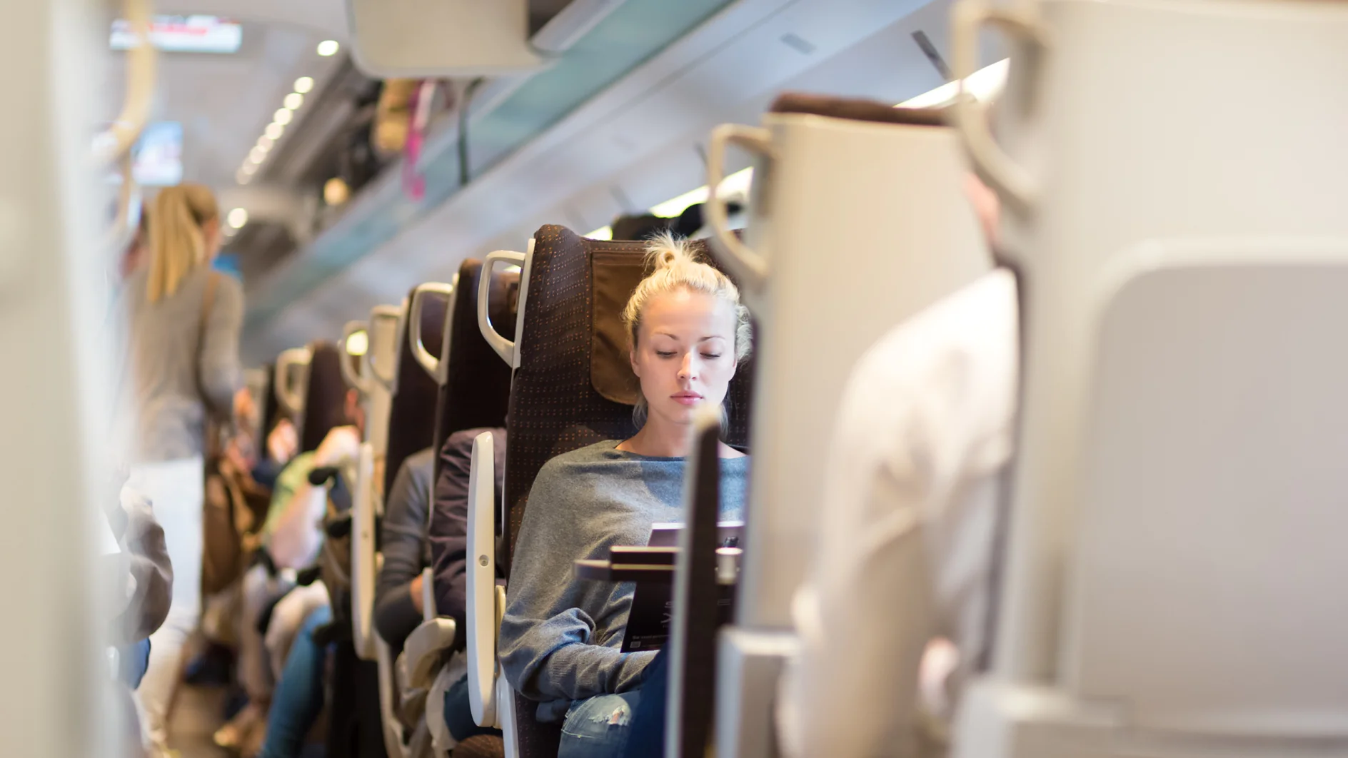 Blonde casual caucasian lady traveling by train. Train full of passengers going to work by public transport at rush hour. Adobe stock image