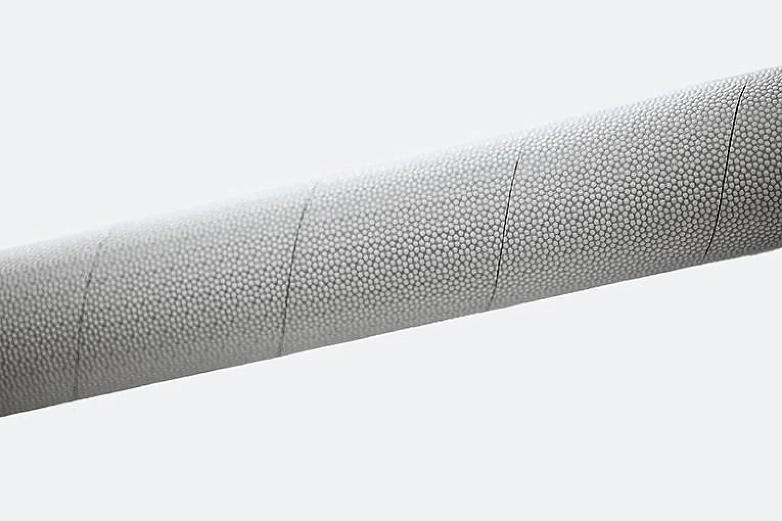 Close-up image of a textured cylindrical object. The surface features a uniform pattern with small, circular, raised elements covering the entirety of the visible area. The objects color is light gray, and it is positioned diagonally against a plain background, resembling the quality and precision you might find in tesa tape products. (This text has been generated by AI)