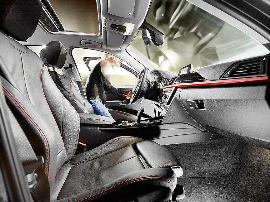 A person is getting into the driver’s seat of a car with a sunroof and black leather interior. The dashboard features a modern design with a small screen. The focus is on the sleek and spacious interior, where tesa tape might be used for securing or repairing components within the vehicle.