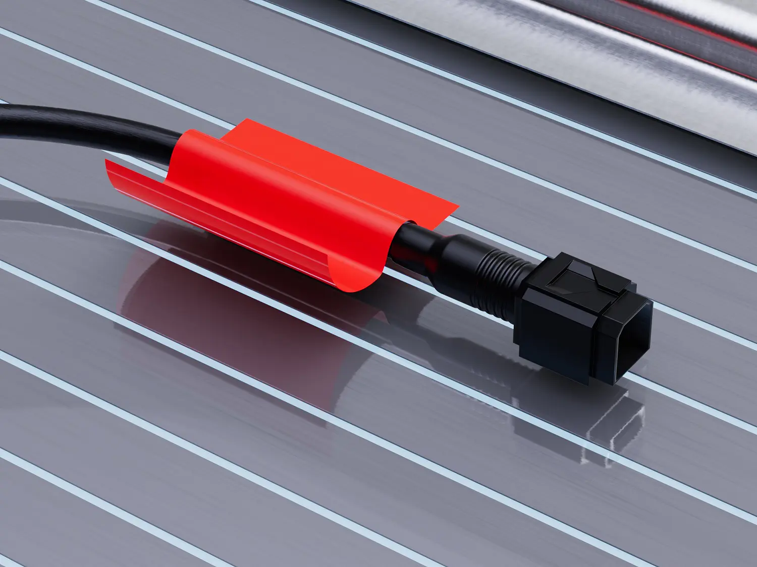 A black cable with a connector is wrapped in a red protective sheath, lying on a metallic, grooved surface. The grooves in the surface run parallel to the cable. The background is a light sky blue. (This text has been generated by AI)