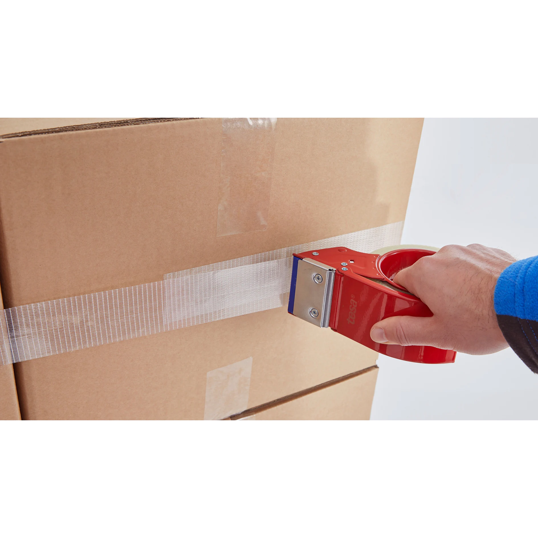 hand using red tape dispenser to seal cardboard box with clear tesa tape in indoor setting (This text has been generated by AI)