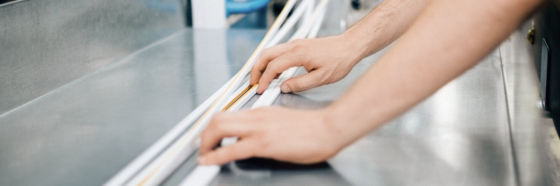hands measuring and aligning white strips on a metal surface in an industrial setting with machinery in the background tesa
