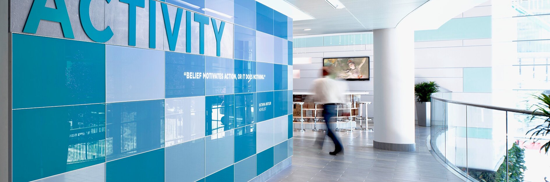 modern indoor hallway with large orange and beige tiled wall displaying "activity" in bold letters, person walking in background