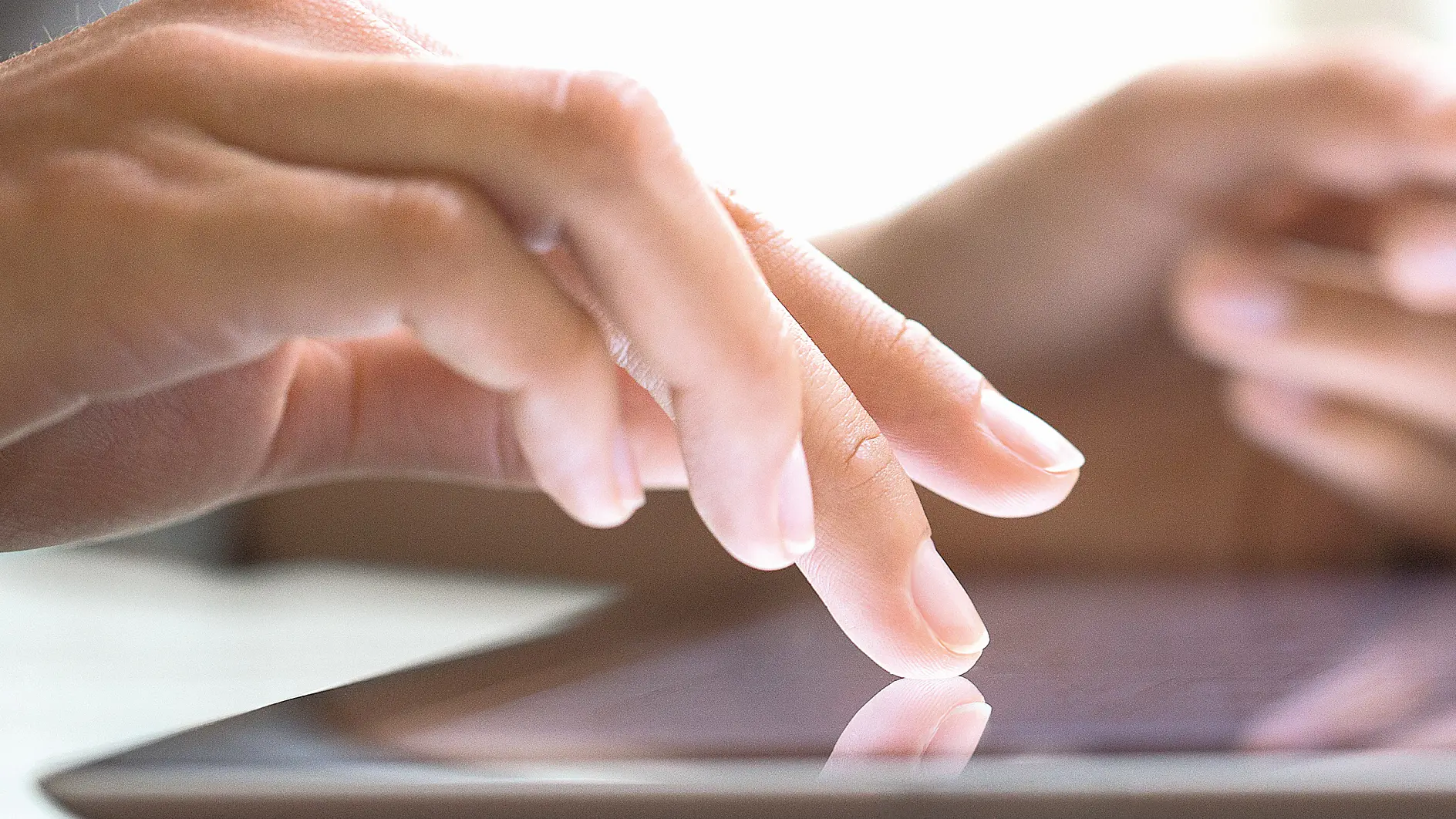 hands tapping on a tablet screen indoors, focusing on finger interaction with the device's touchscreen