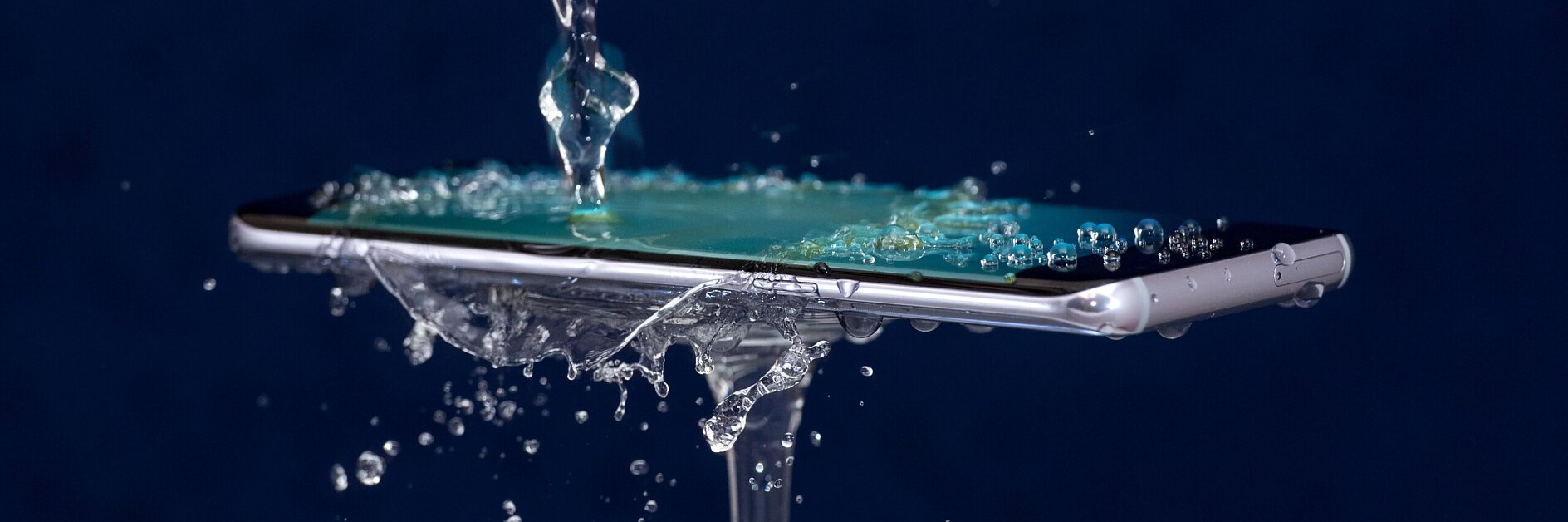 smartphone held horizontally outdoors with water pouring over its screen, demonstrating water resistance capabilities