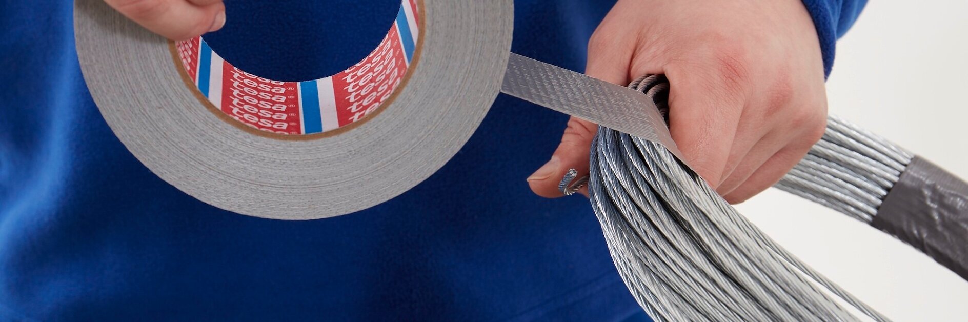 Hands wrapping tesa bundling tapes around a bundle of metal wires on a white background.