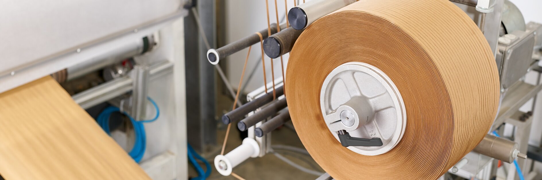 roll of brown packing tape mounted on dispenser in industrial packaging area with conveyor belt and tools nearby