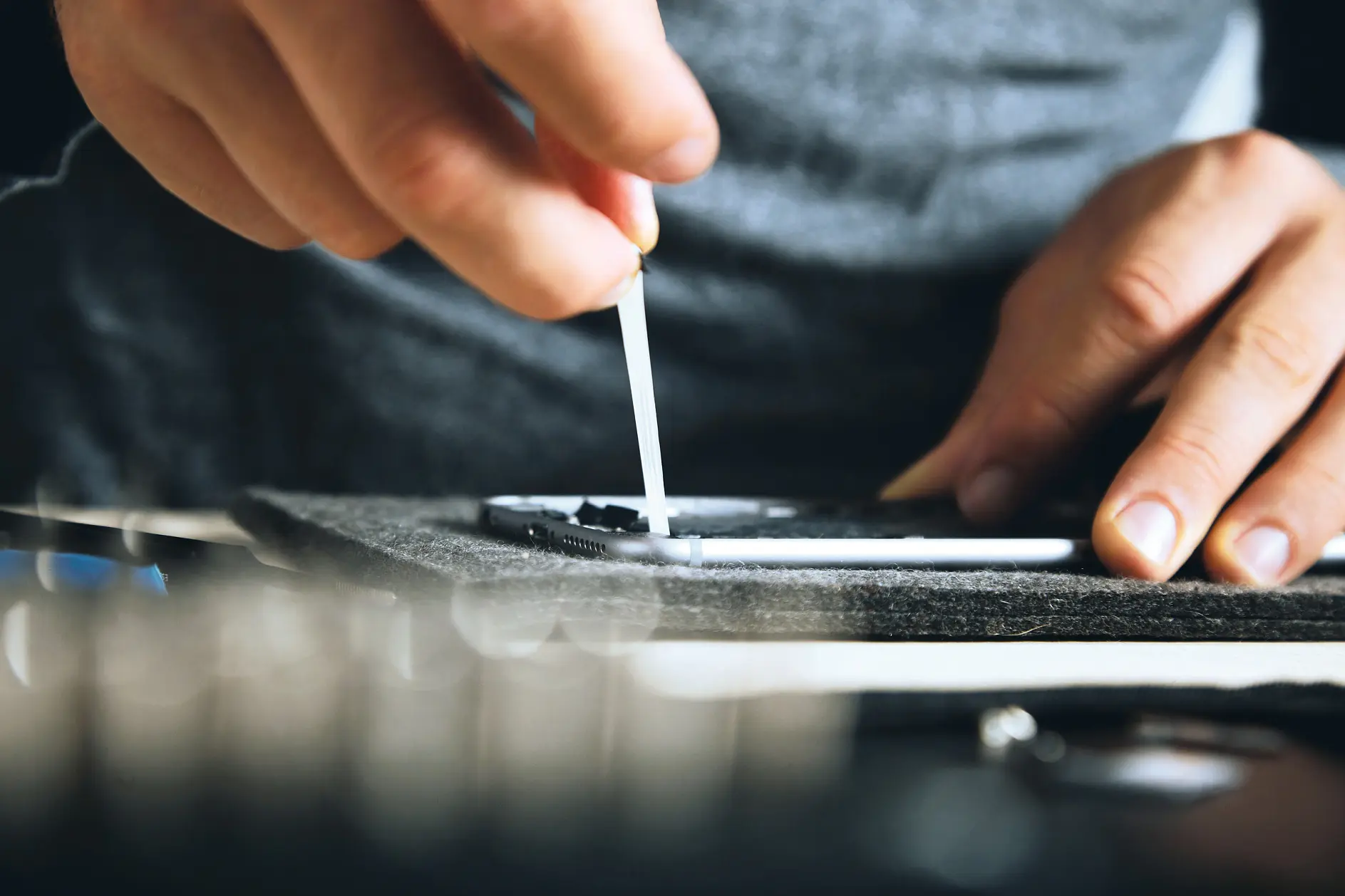 hands applying black adhesive with a small tesa tape strip on a gray fabric surface in an indoor workspace