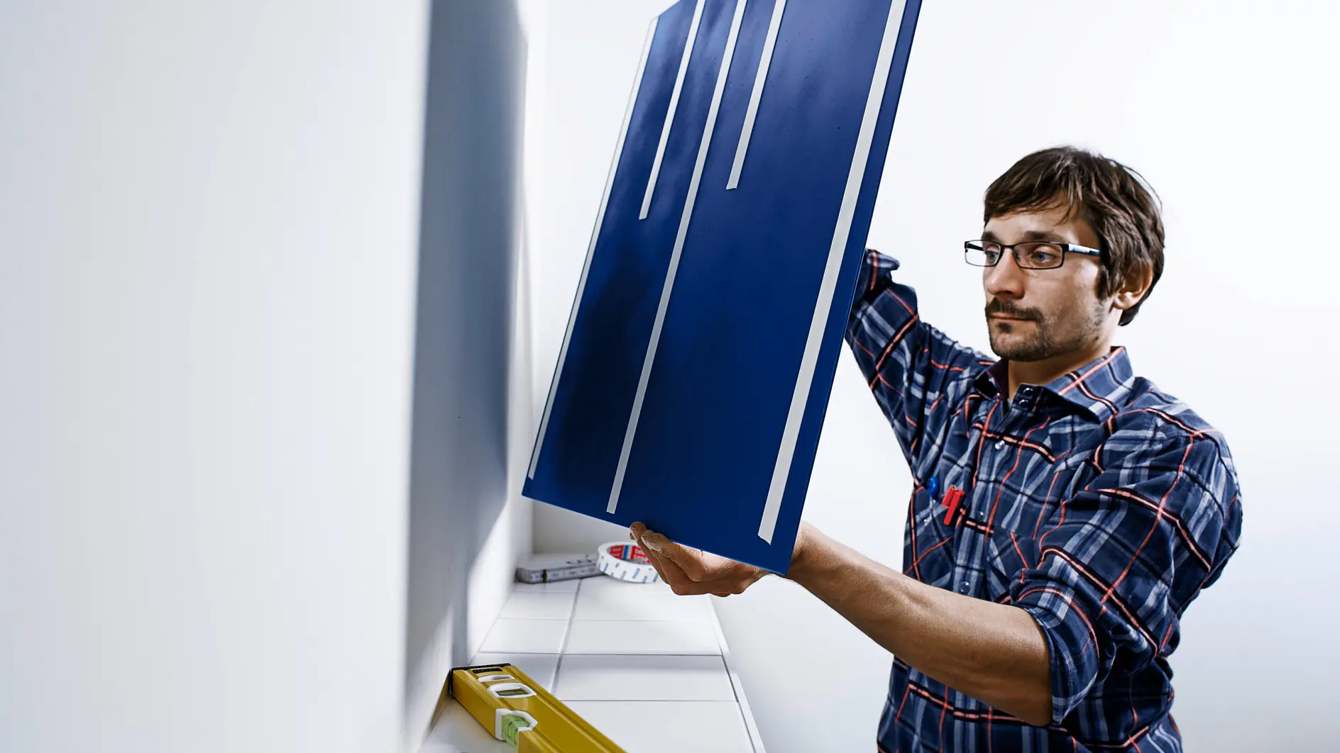 A man mounting a mirror on a wall using the strongest removable mounting tape from tesa®, achieving secure bonding without drilling or screws.