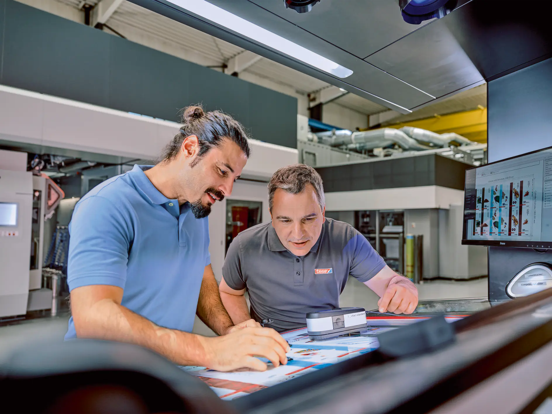 two men in a workshop setting reviewing documents and working with tools on a table under industrial lighting (This text has been generated by AI)