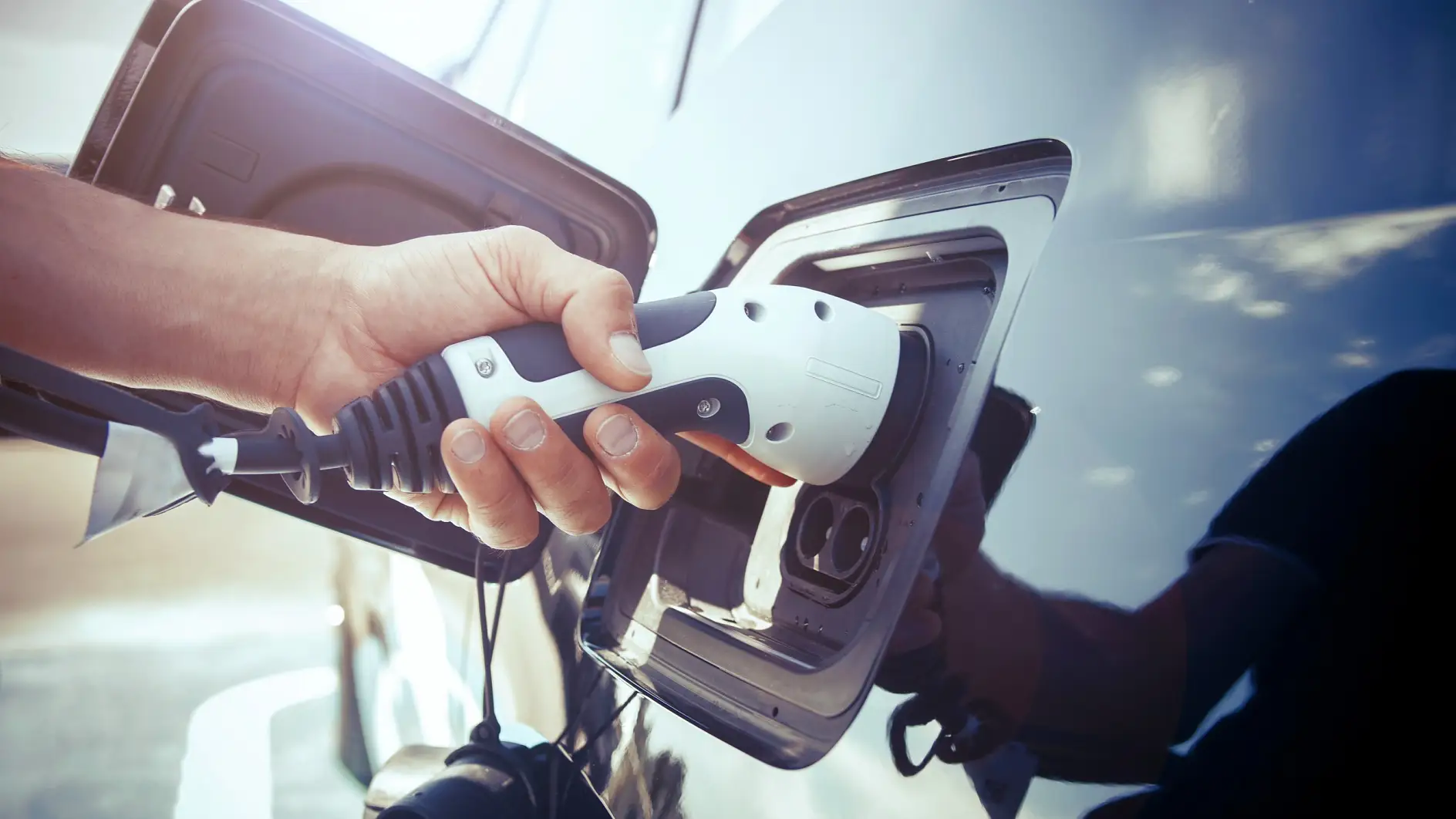 Color image of a man's hand preparing to charge an electric car.