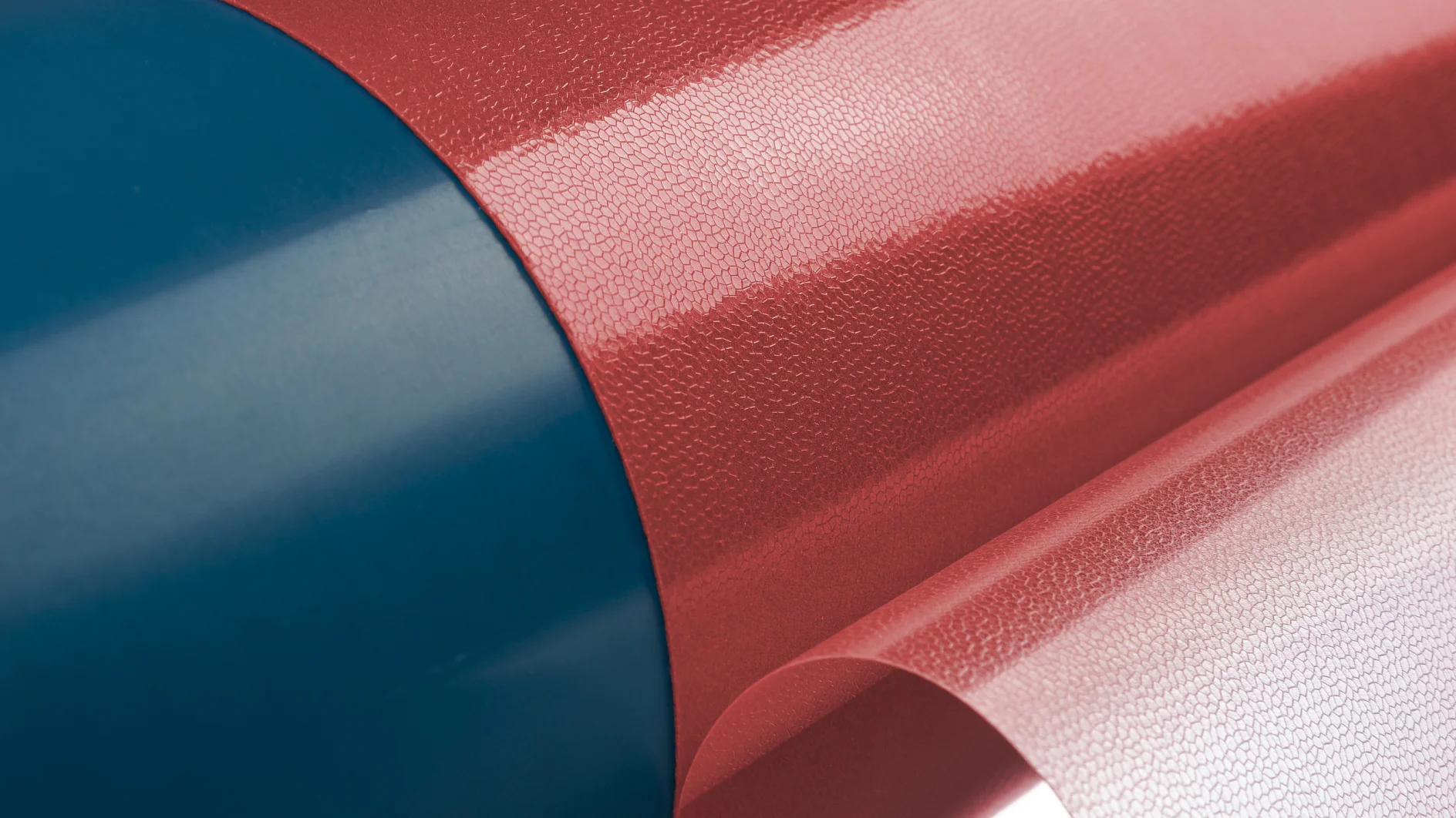 Close-up of a roll of reflective material with a red and blue cylinder. The sheet is partially unrolled, showing a shiny, textured surface on a white background, secured with tesa tape. (This text has been generated by AI)