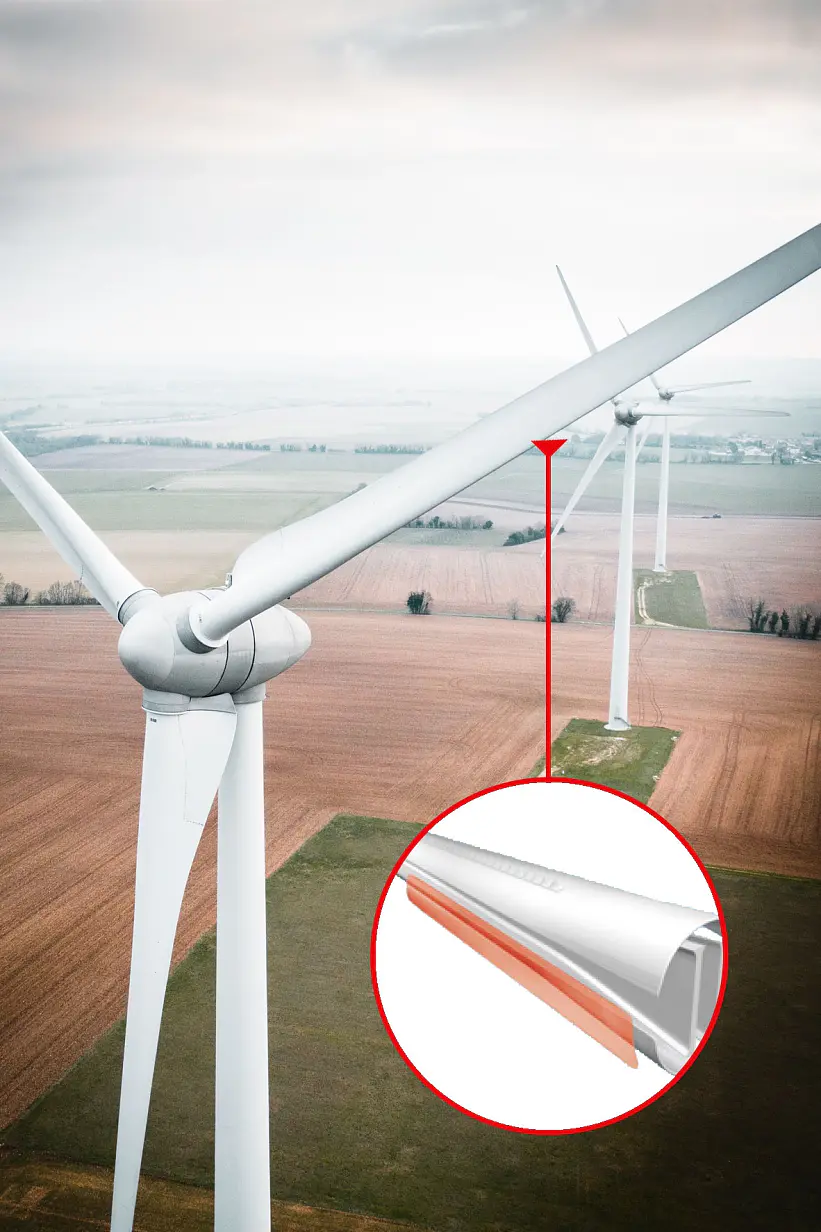 Aerial view of a wind turbine in a field, with a close-up inset of the turbine blades edge. The turbine is surrounded by agricultural land under a cloudy sky.