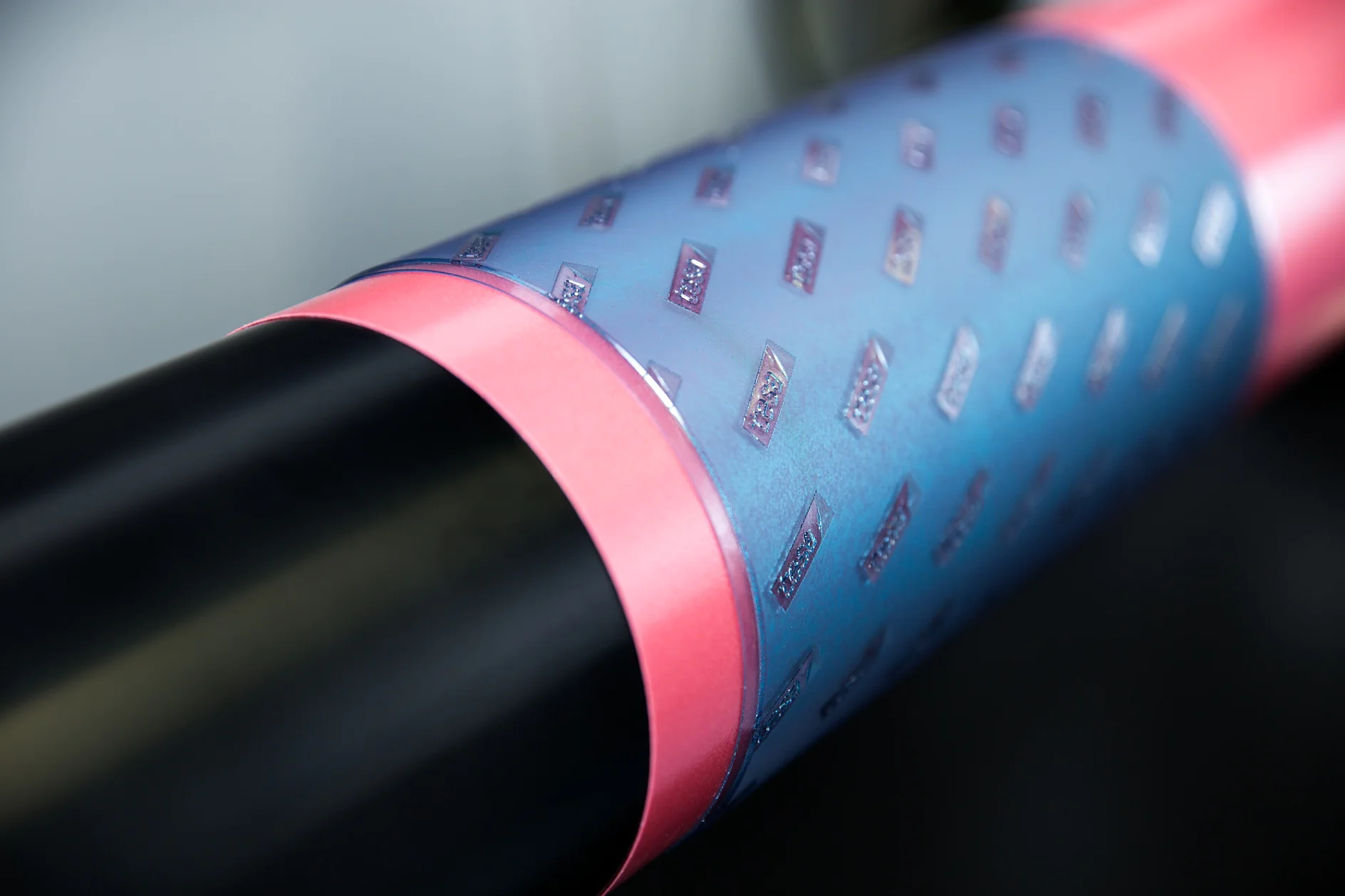 Close-up of a cylindrical object with a black section and a metallic blue section covered in a raised pattern of small rectangles. A pink band separates the two sections. The surface appears glossy and reflective, all held together seamlessly by tesa tape. (This text has been generated by AI)