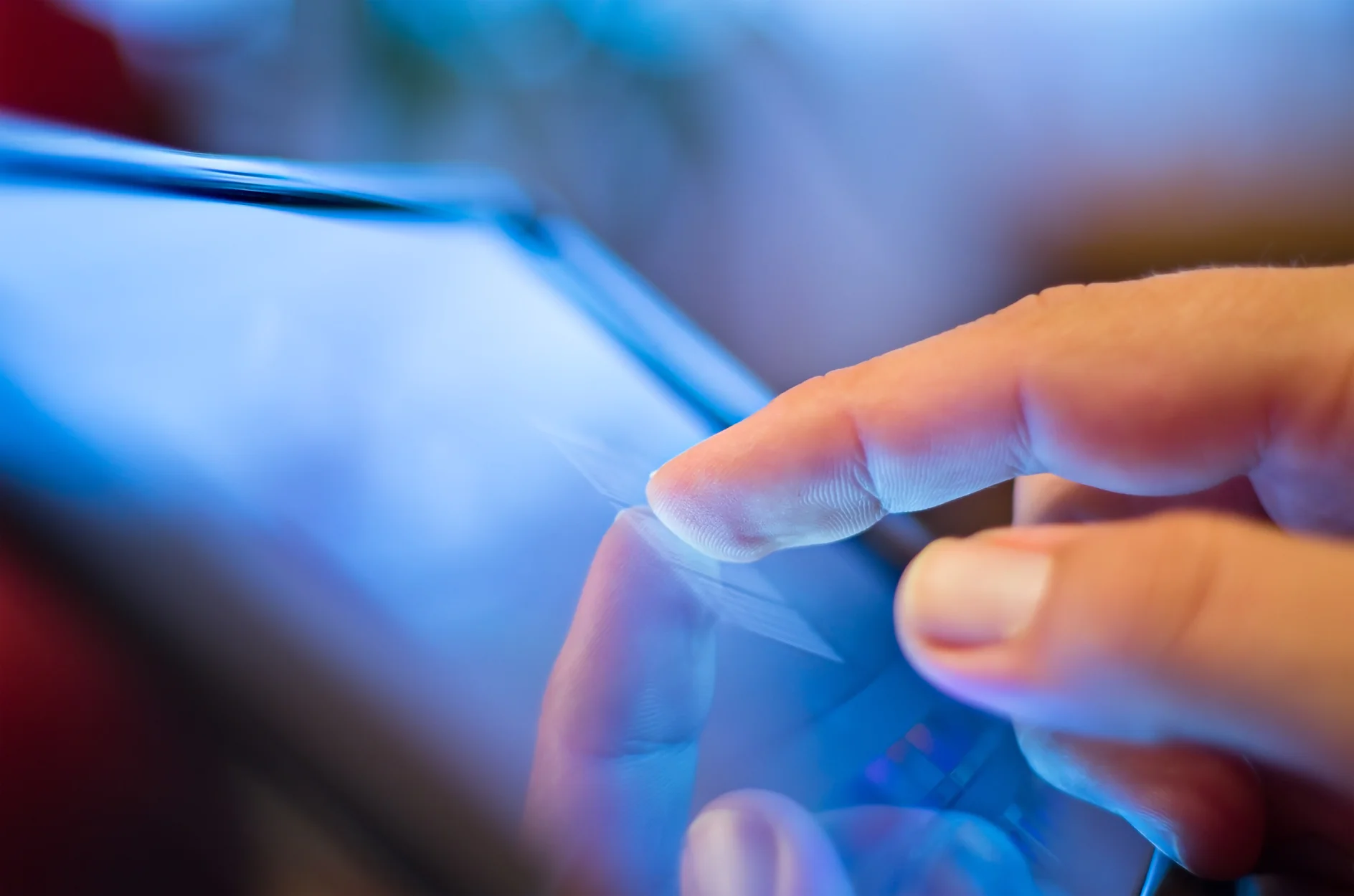 A close-up of a persons finger tapping on a touchscreen device, possibly a tablet or smartphone. The screen emits a blue light, and the background is blurred. (This text has been generated by AI)