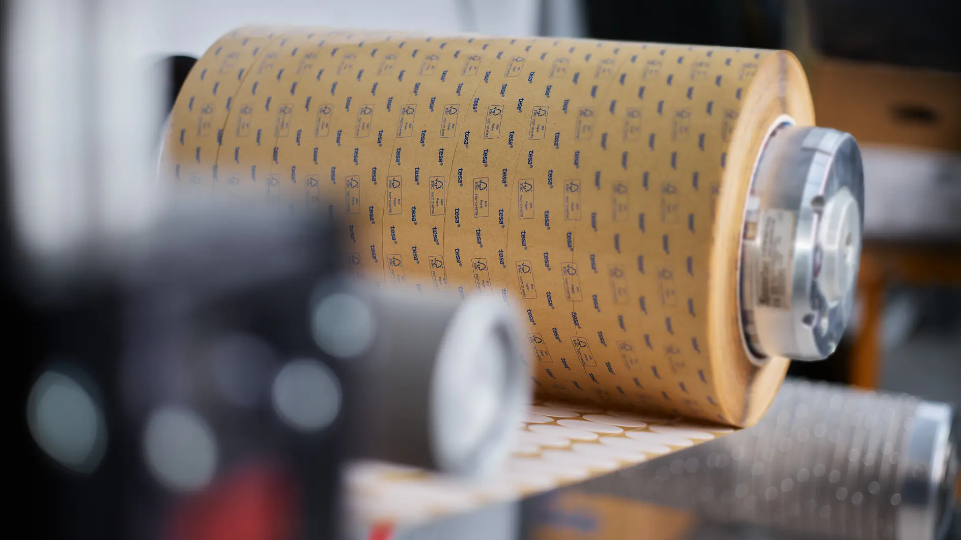 roll of tesa adhesive tape with printed logo on a dispenser in an indoor industrial setting (This text has been generated by AI)
