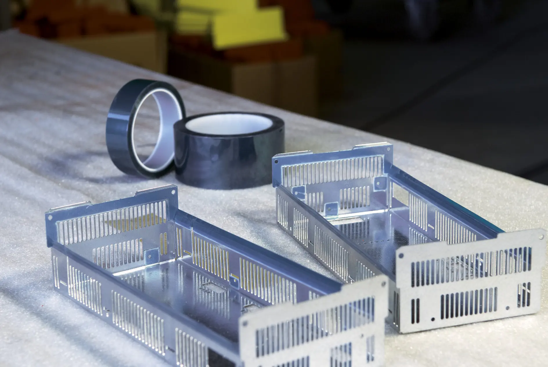 two metallic enclosures and rolls of tape are placed on a work surface.
