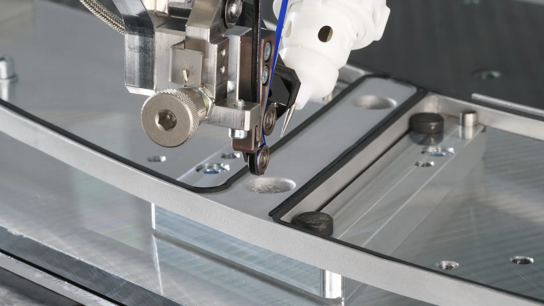 close-up of industrial sewing machine stitching gray fabric on metal table in indoor manufacturing setting