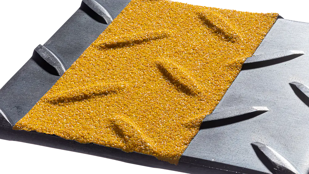 Close-up of a textured surface containing a yellow, gritty area with diagonal ridges, bordered by sections of dark gray metal with parallel grooves. The contrast highlights the different materials and textures. (This text has been generated by AI)