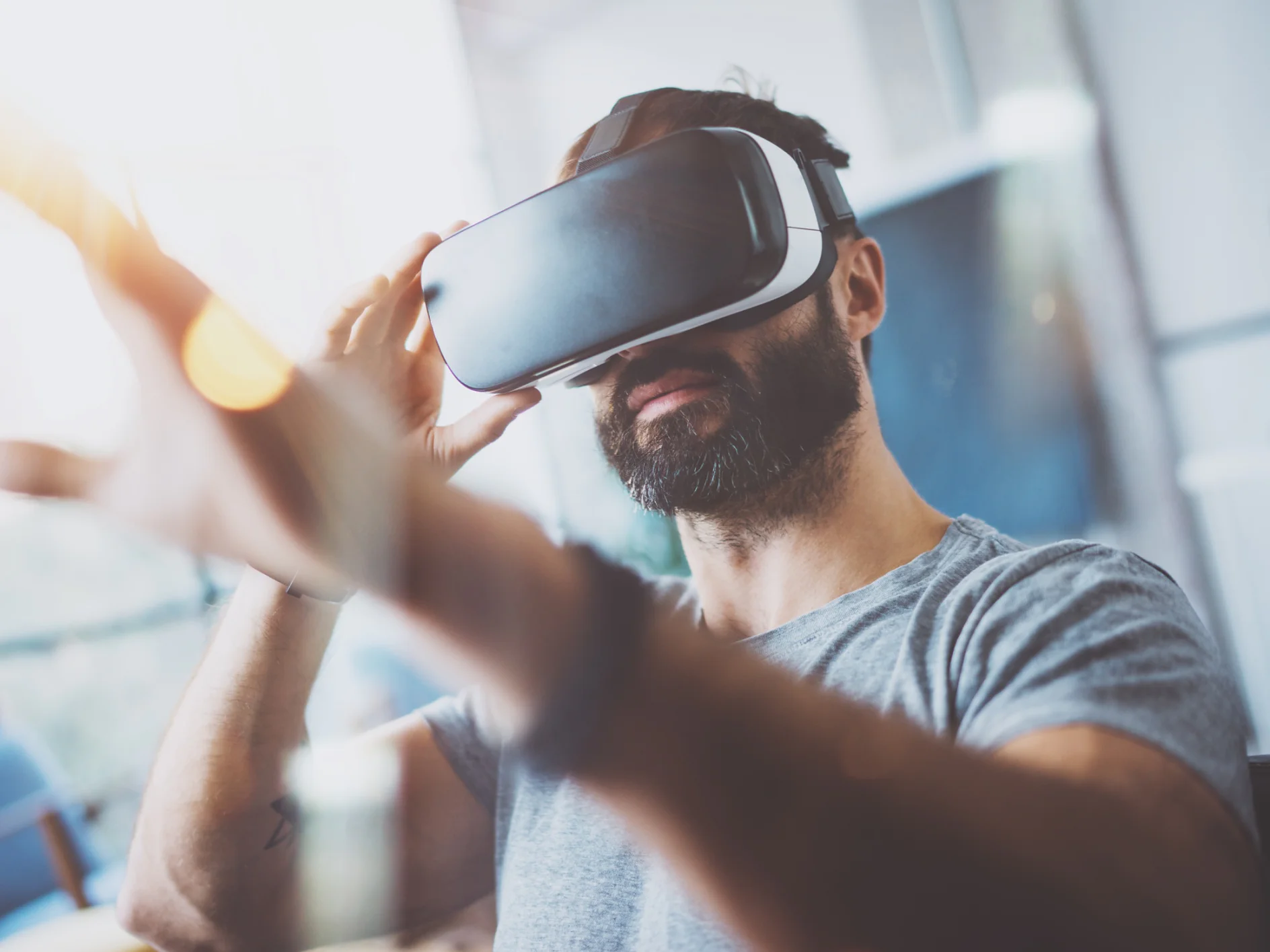 Closeup of bearded young man wearing virtual reality goggles in modern coworking studio. Smartphone using with VR headset. Horizontal, blurred