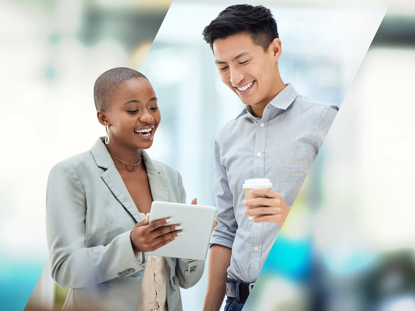 Two people stand side by side, smiling and engaging with a tablet. The person on the left holds the tablet, while the person on the right holds a cup. Both are dressed in business attire with a blurred office background. There is no mention of tape in this text to replace with tesa tape. (This text has been generated by AI)