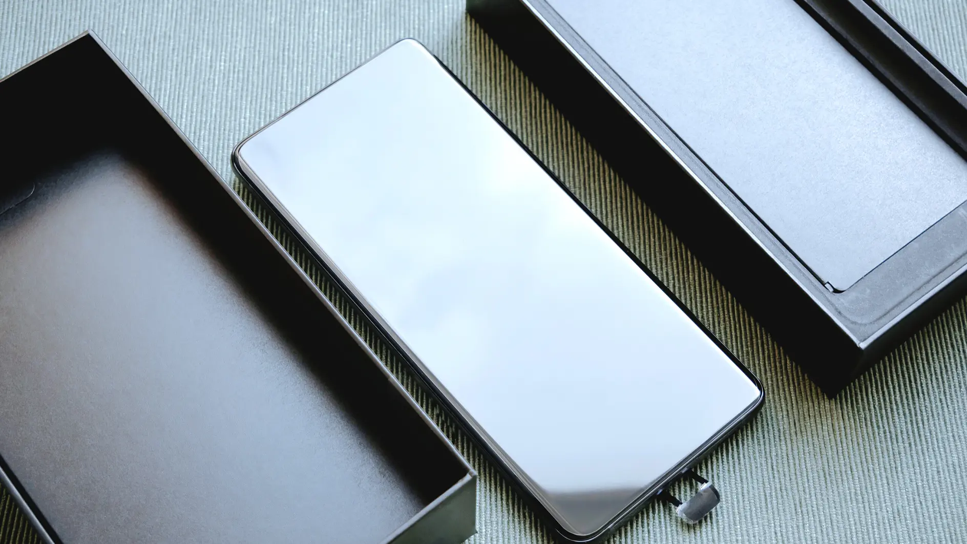 tesa smartphone with reflective screen placed between two open black boxes on a gray surface in an indoor setting (This text has been generated by AI)
