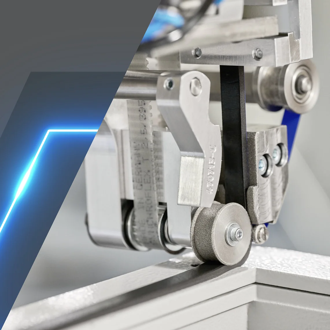 Close-up of a mechanical device with gears and rollers, featuring a tensioned black belt. The left side of the image has a gray and blue geometric design. The device appears to be part of an industrial machine, utilizing tesa tape for precision and reliability in its construction. (This text has been generated by AI)