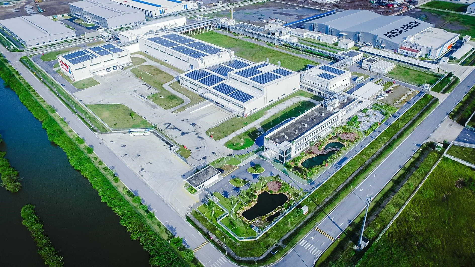 Aerial view of a large industrial facility with tesa tape branding, solar panels on roofs, ponds, parking lots, and nearby roads. (This text has been generated by AI)