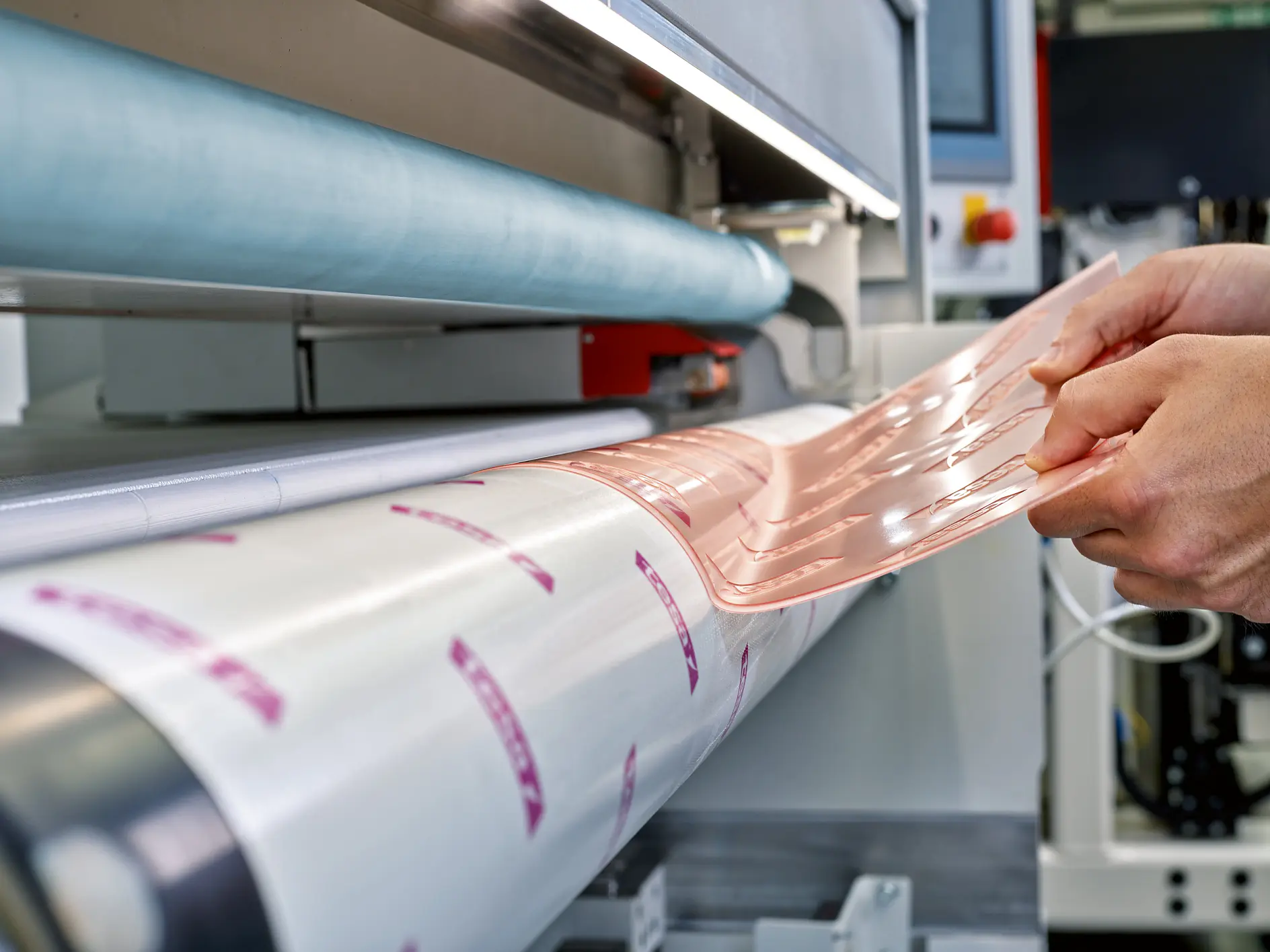 tesa branded adhesive tape being applied to a roll in an industrial setting with machinery and hands visible
