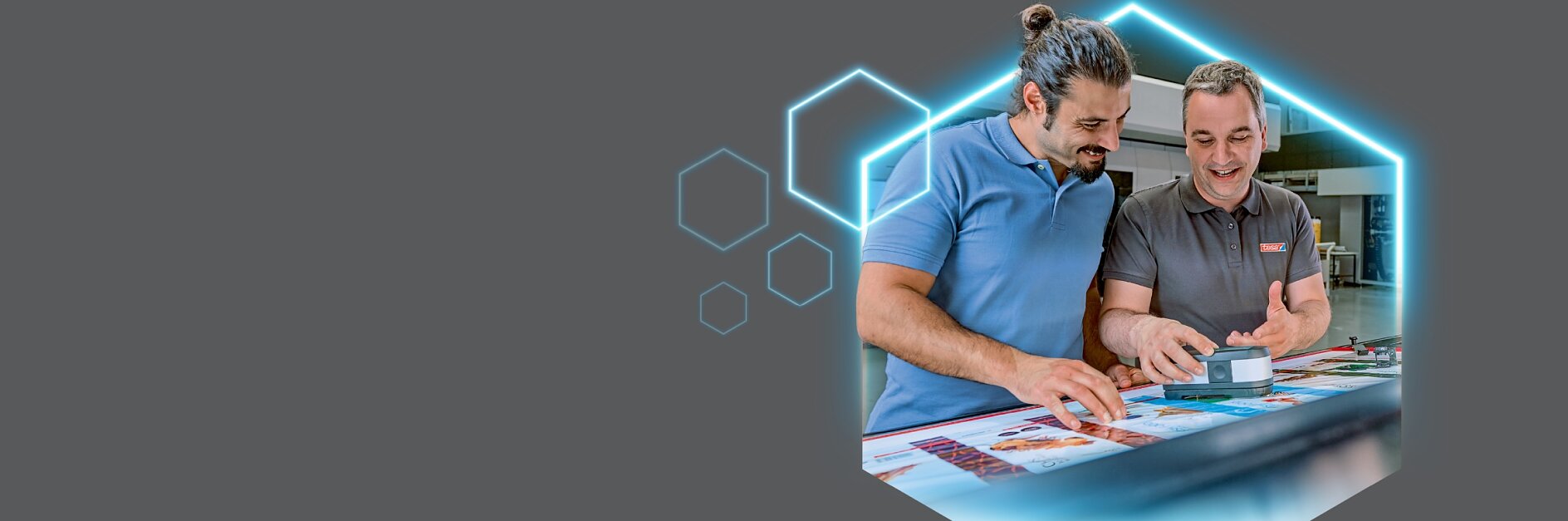 Two men at a table discuss printed materials, possibly about tesa tape; one wears blue, one gray. Blue hexagons on gray background.