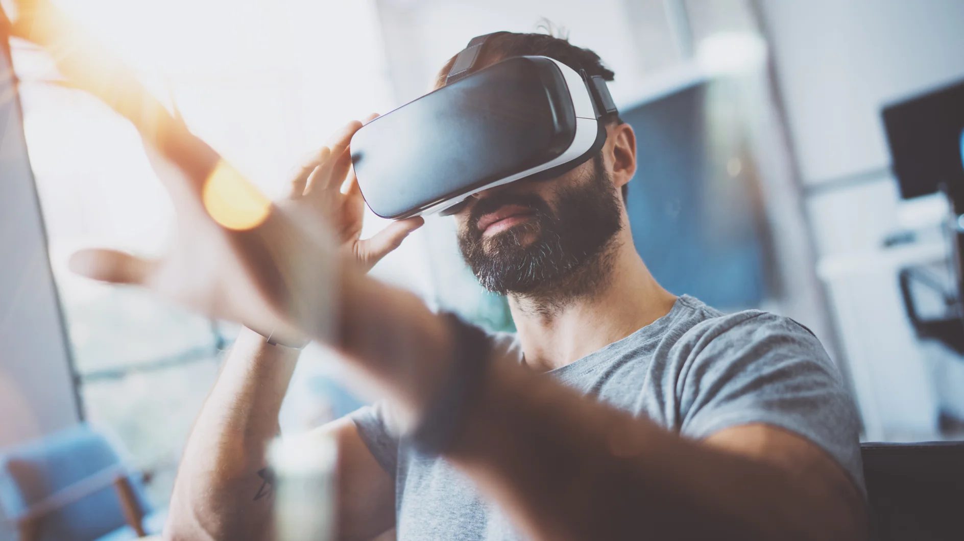 Closeup of bearded young man wearing virtual reality goggles in modern coworking studio. Smartphone using with VR headset. Horizontal, blurred