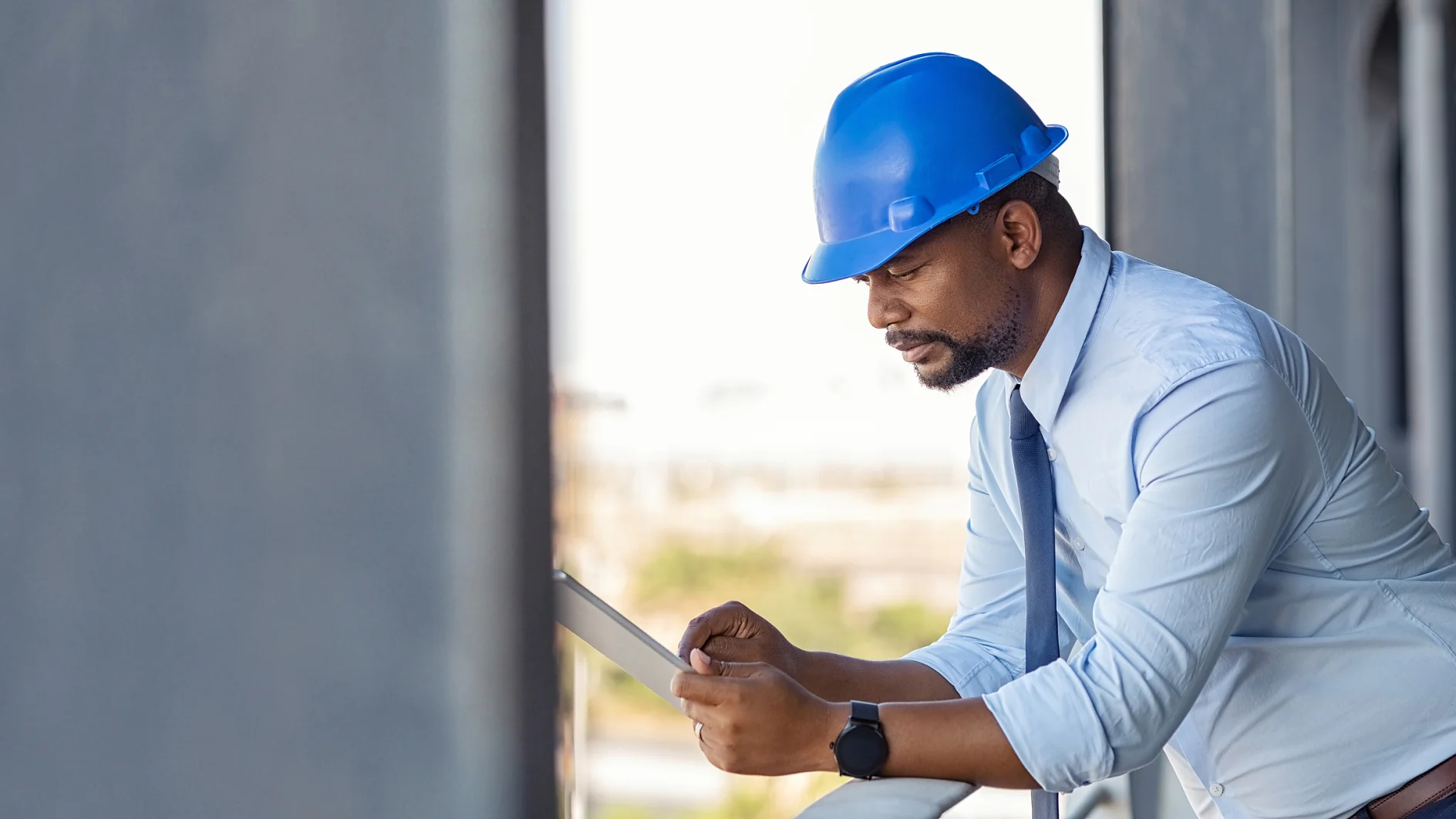 A construction worker on an upper floor of a building site, wearing a blue helmet, leaning on the scaffolding with one arm and holding a paper that he is inspecting, with possible construction tapes visible in the background. Photo: Daniel Sumesgutner