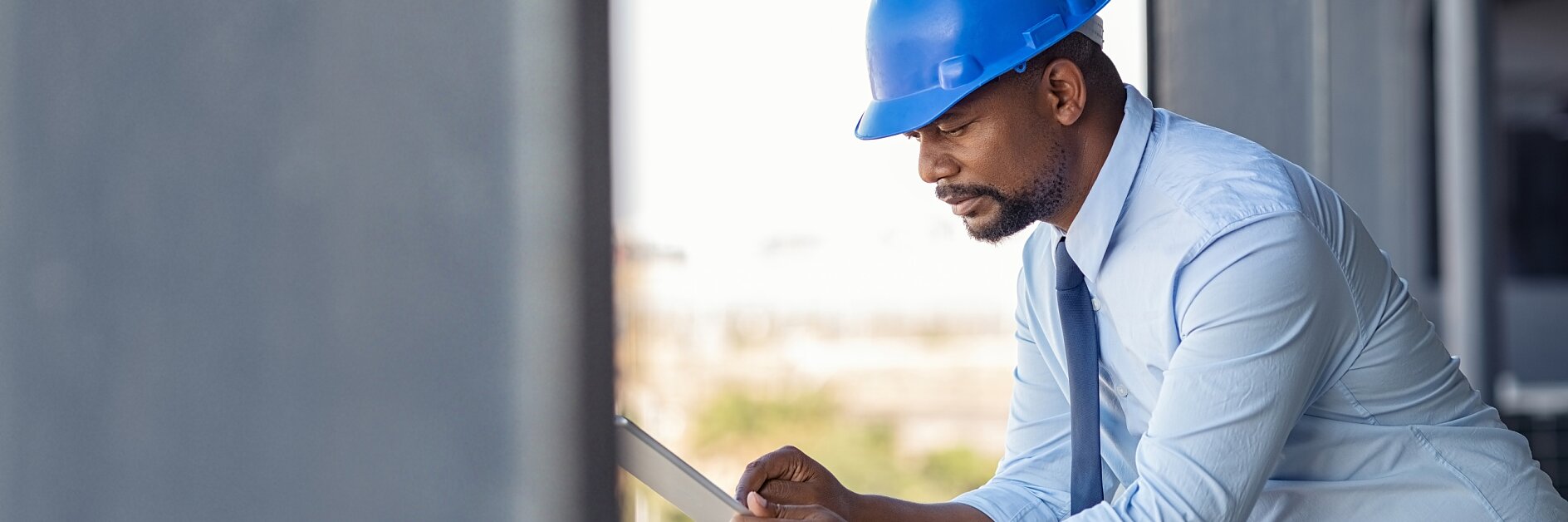 A construction worker on an upper floor of a building site, wearing a blue helmet, leaning on the scaffolding with one arm and holding a paper that he is inspecting, with possible construction tapes visible in the background. Photo: Daniel Sumesgutner