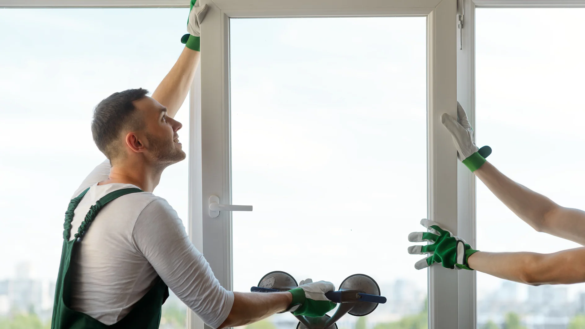 Photo of two workers installing a plastic window. Man holding a glass pane with a vacuum lifter.